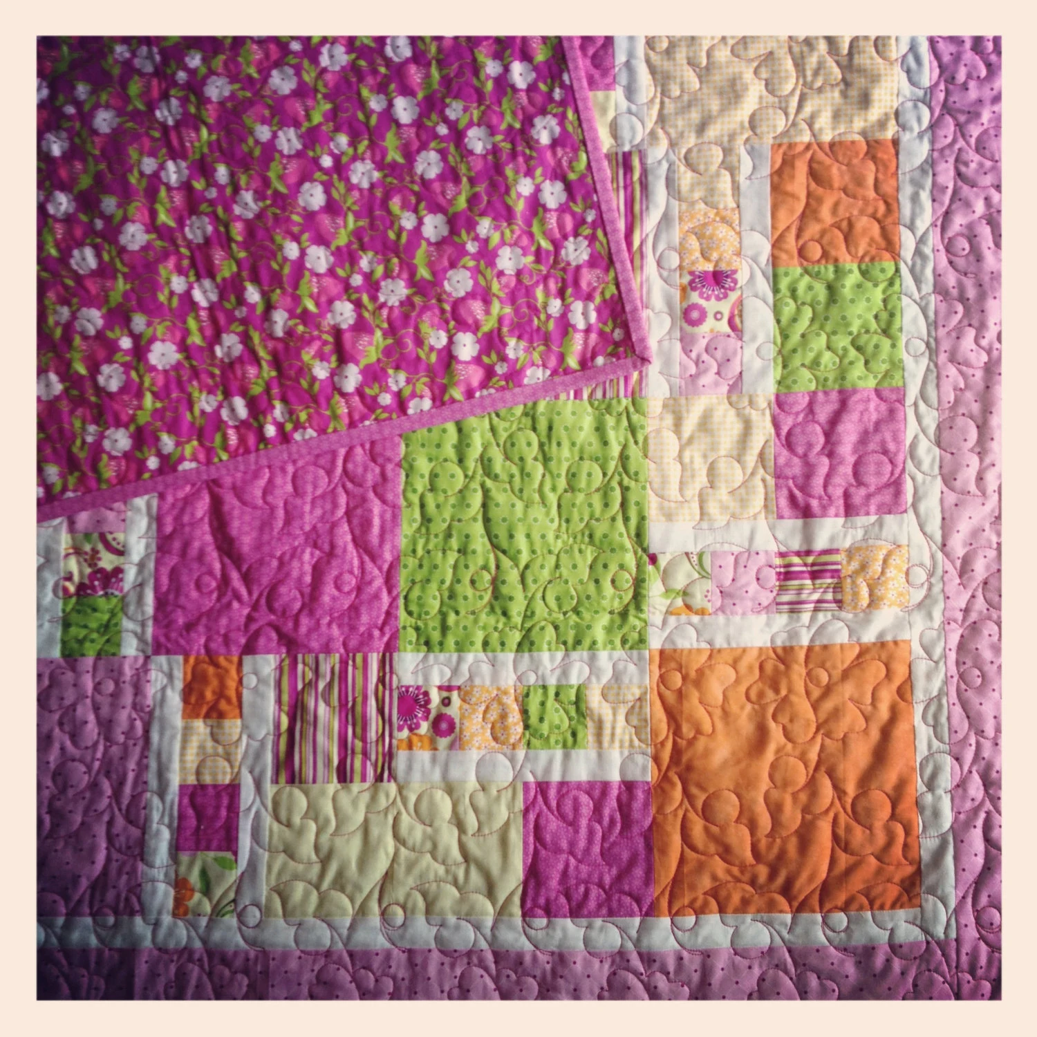 Close-up of a patchwork quilt corner folded back to reveal a floral pink backing fabric, with pink, green, orange, and cream squares, soft handmade mood.