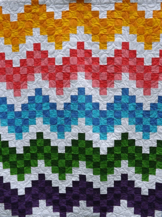 Close-up of a zigzag patchwork quilt in rainbow stripes of yellow, red, blue, green and purple on white, vibrant and colorful textile artwork