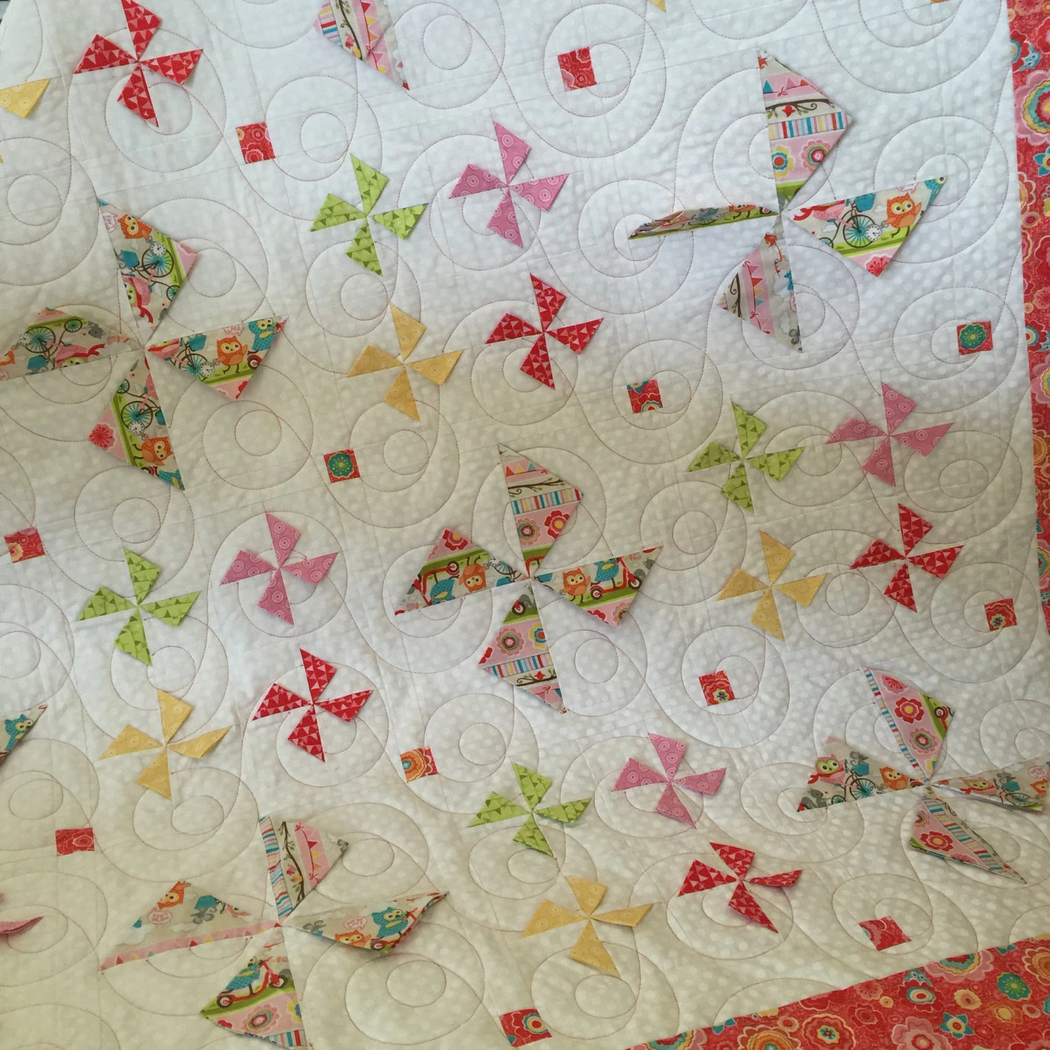 White quilted fabric background dotted with small pinwheel fabric accents in pink, green, red, and cream, conveying a soft handmade mood